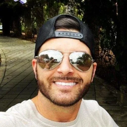 Tony Lea, smiling, in a backwards cap and aviator sunglasses