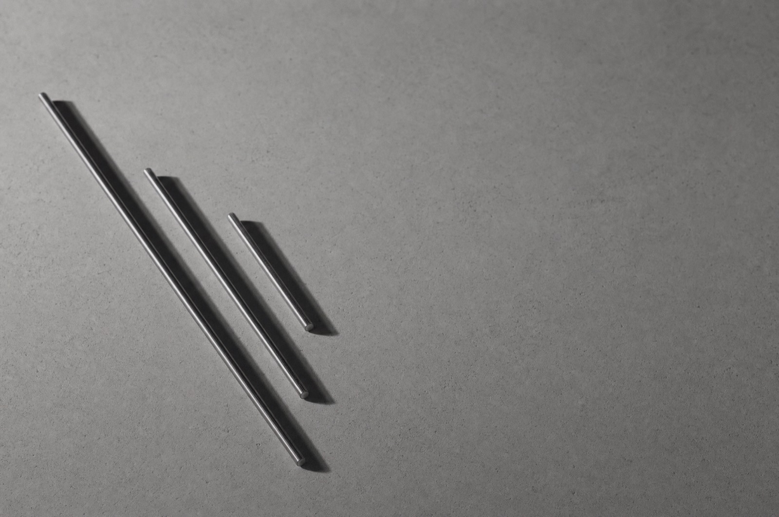 Three thin steel rods lying parallel on concrete, casting crisp shadows