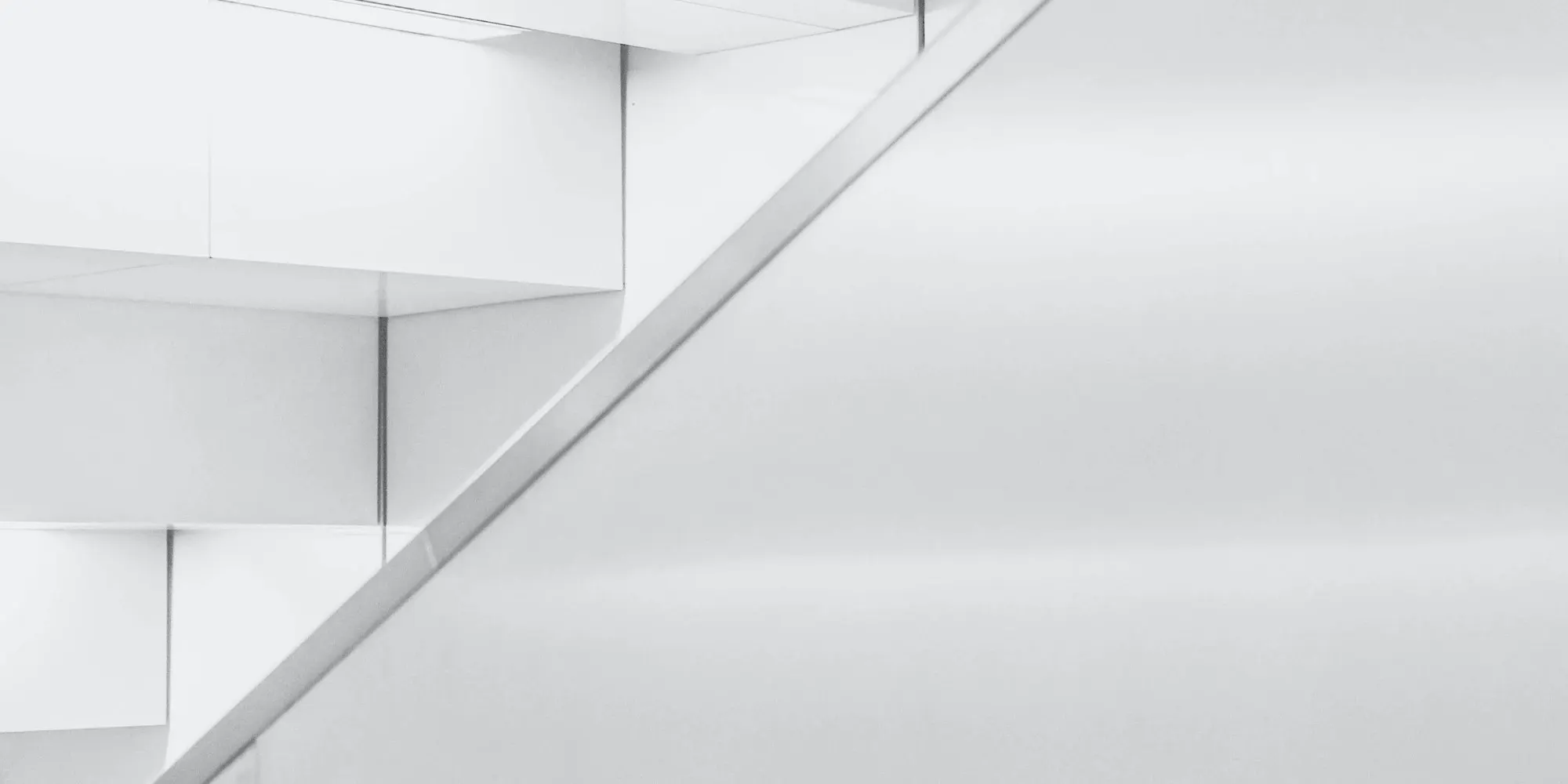 A white staircase and steel handrail climbing across a pale wall