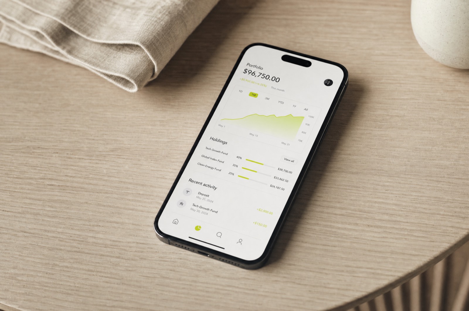 A smartphone on a pale oak desk showing a minimal finance dashboard