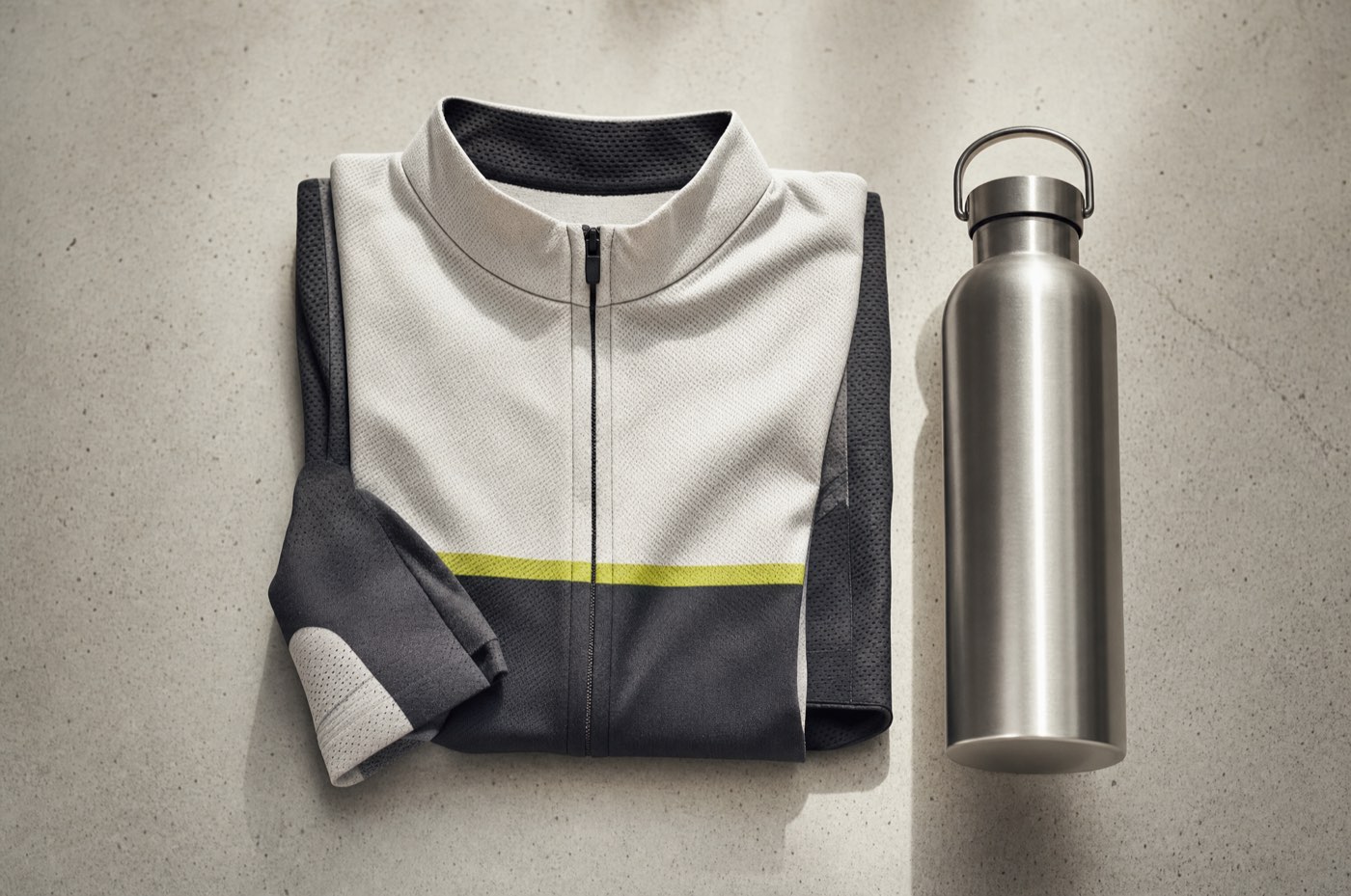 A folded technical cycling jersey beside an aluminium bottle, overhead view