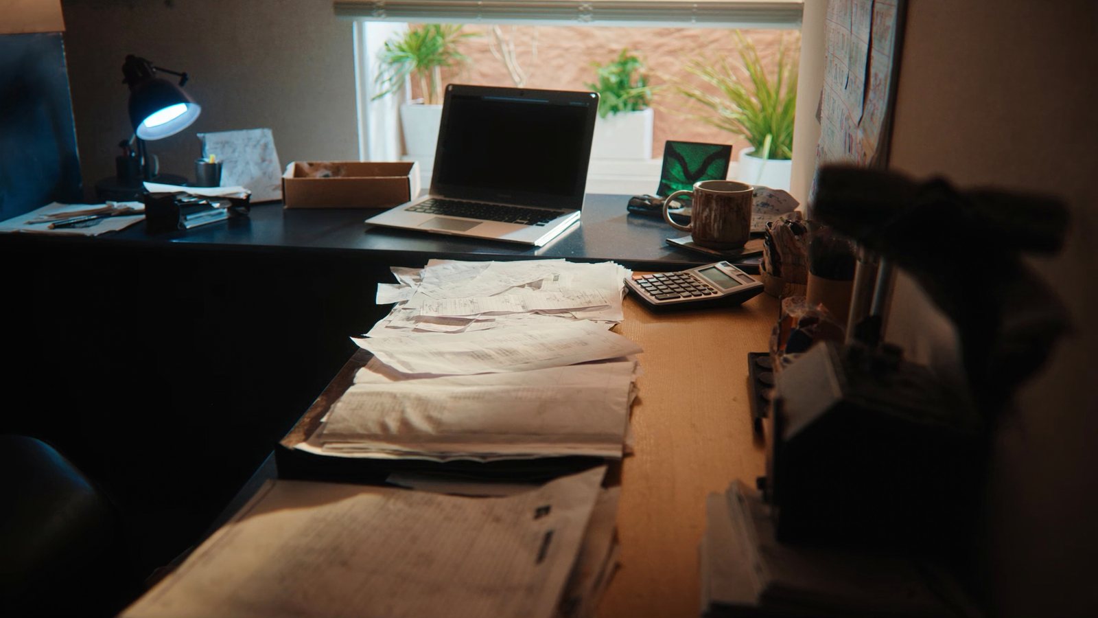 A sunny home office with stacked receipts, a calculator and a laptop