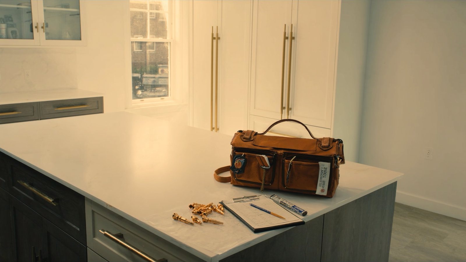 A contractor's tool bag, a clipboard and brass fittings on a bright kitchen counter