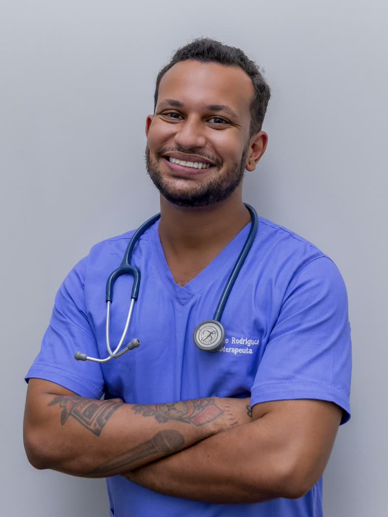 A clinician in blue scrubs with a stethoscope, arms folded, smiling