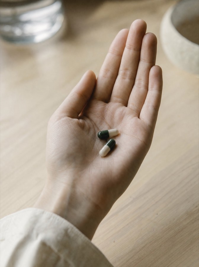 Two capsules held in an open palm above a wooden counter